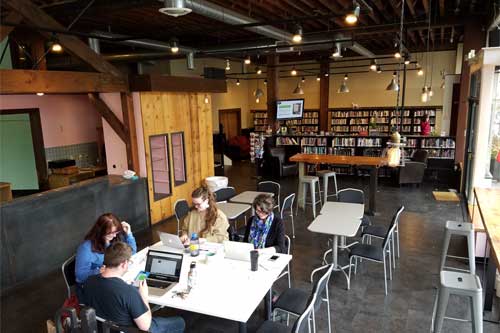 A photo of Gay City's storefront featuring the LGBTQ library, and members of Three Dollar Bill Cinema getting some work done in the front space.